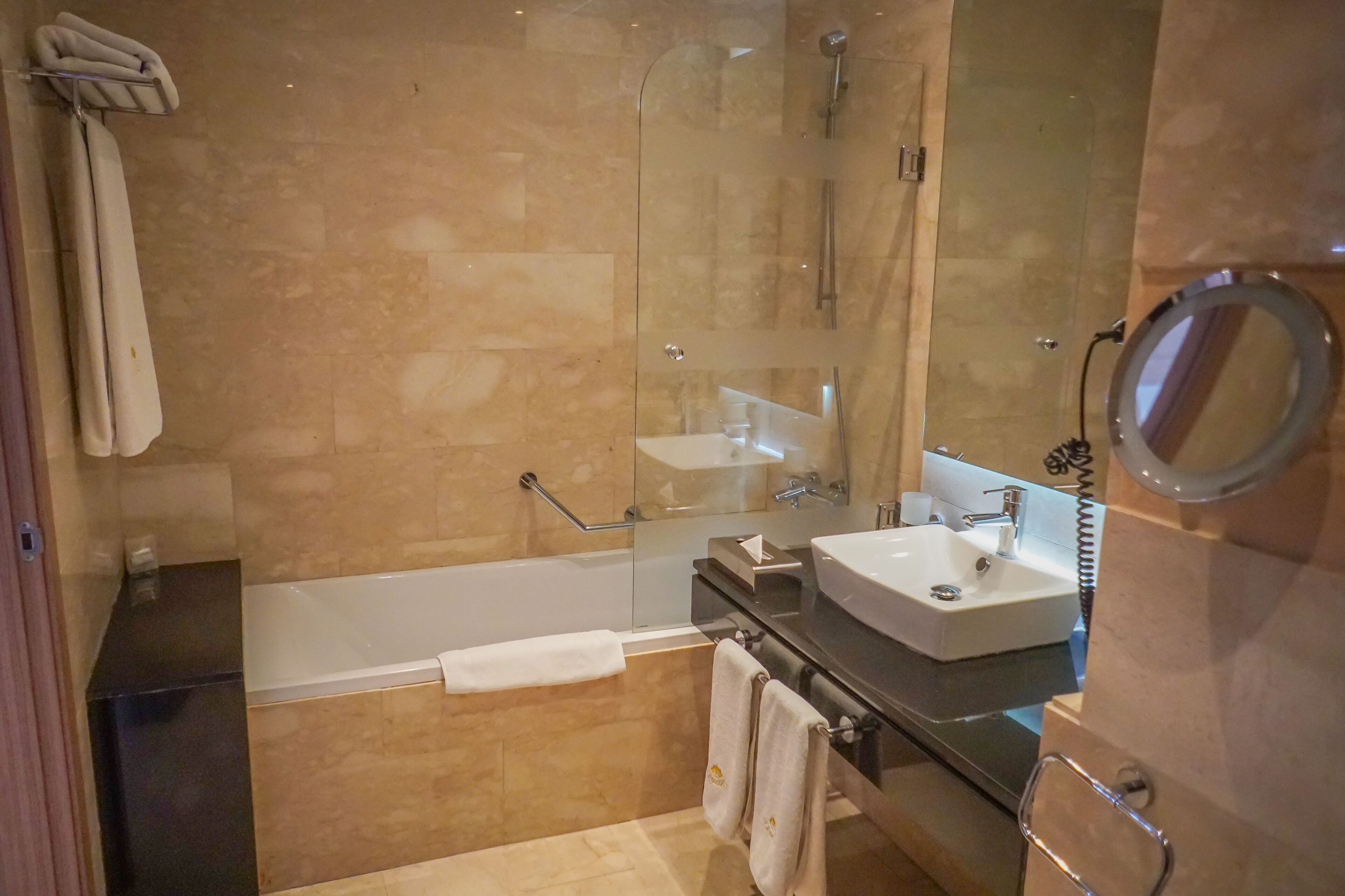 A modern bathroom with a glass-enclosed shower, a white bathtub, a sink with a mirror, and a towel rack.