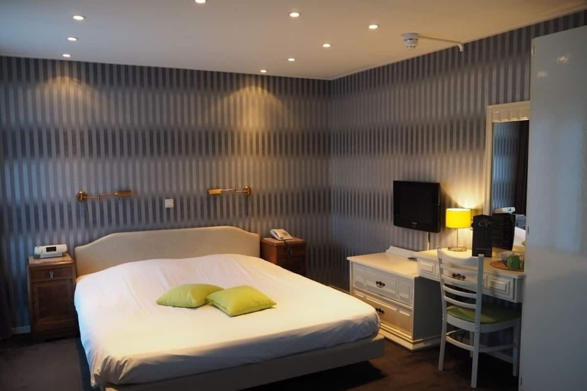 A hotel room with a large bed, a desk with a chair, a television, and a lamp.