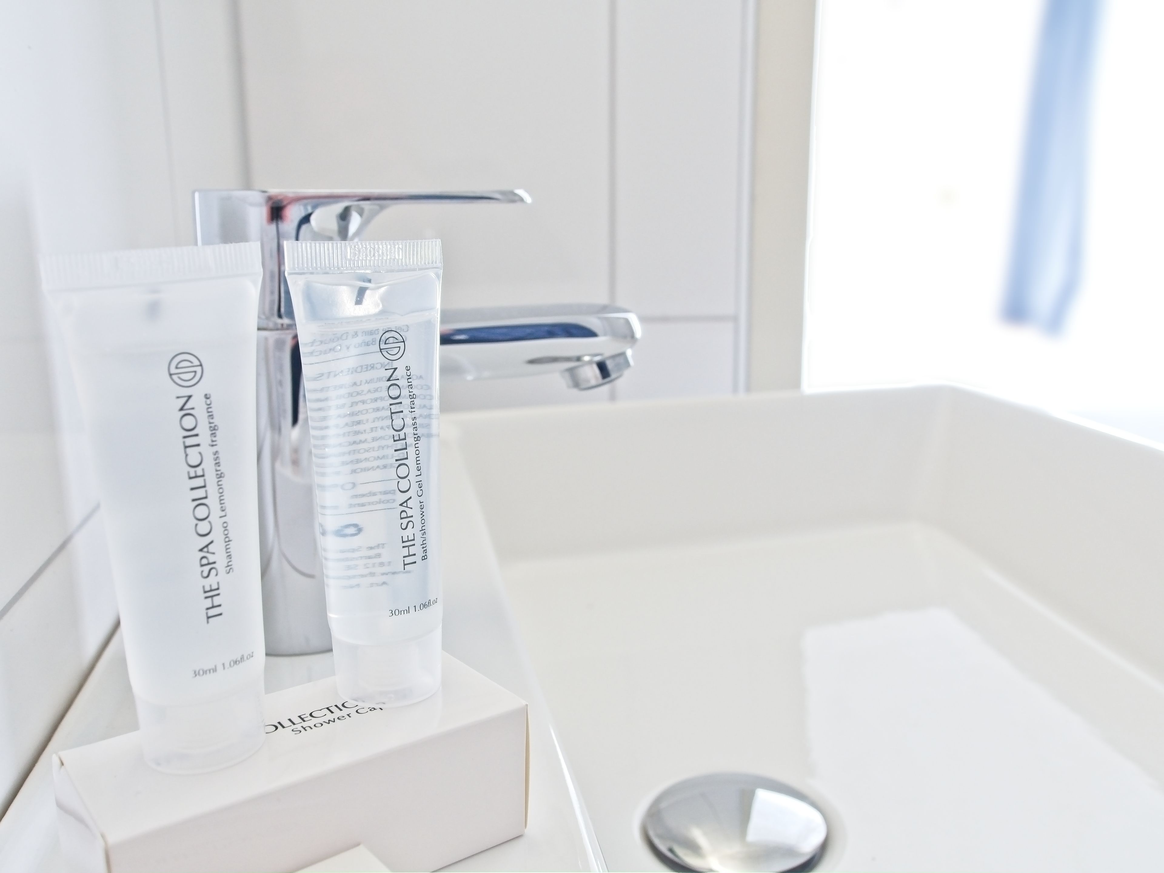 Un baño con un lavabo blanco, un espejo y dos botellas de gel de baño y ducha de The Spa Collection sobre una caja blanca.