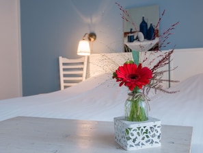 A white bed with a small white table beside it. A glass vase with red flowers and green foliage is placed on the table. - Stadshotel De Graafschap (Doetinchem)