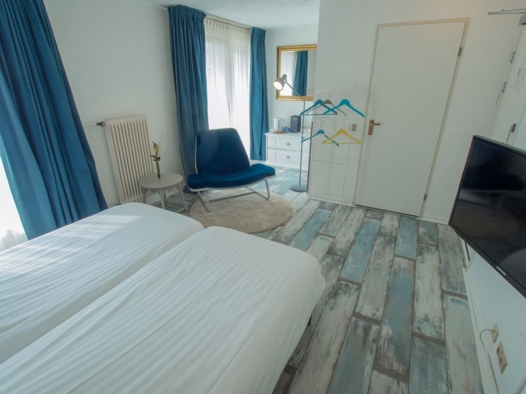 Une chambre d’hôtel comprenant un lit, une chaise, un bureau, une télévision et une armoire avec des cintres.