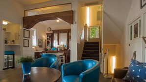 A hotel lobby with a wooden staircase, a reception desk, and seating areas with blue chairs.