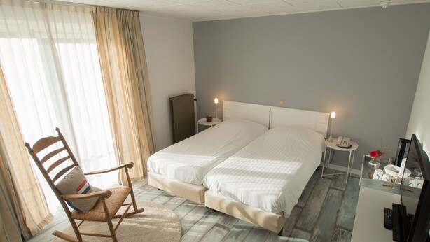 A bedroom with a double bed, a rocking chair, a bedside table with a lamp, and a TV stand with a remote control.