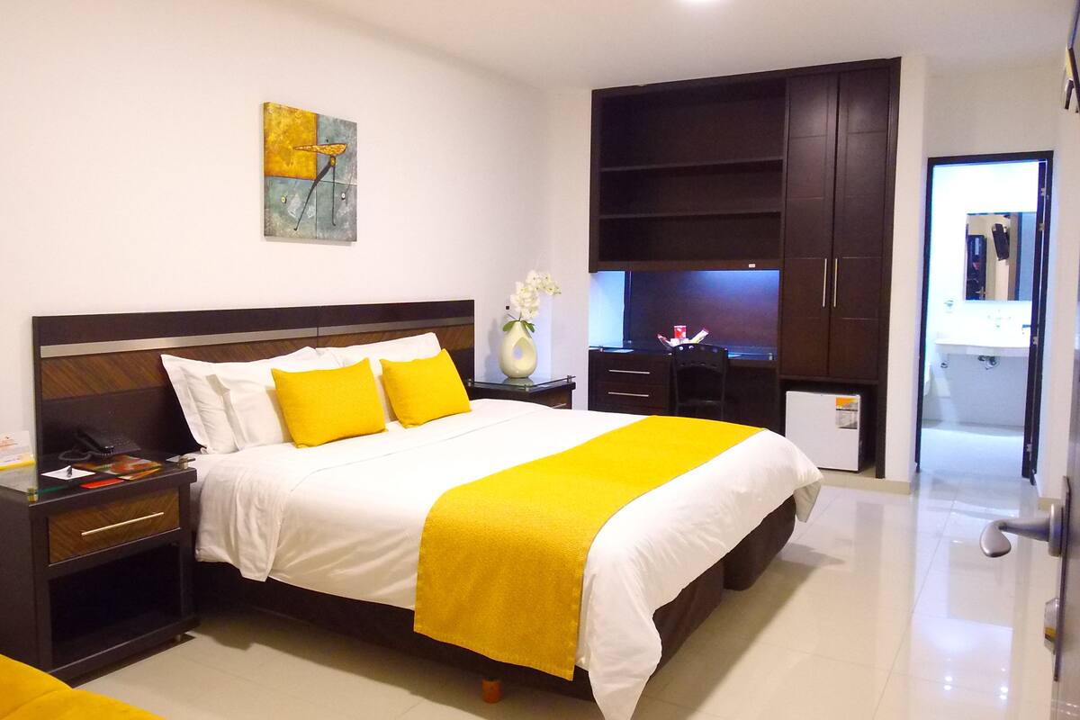 A modern hotel room with a large bed, a desk, and a wardrobe.