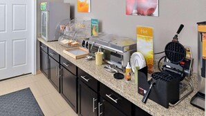 Ein Frühstücksbuffet mit Waffeleisen, Kaffeemaschine und Obstauslage.