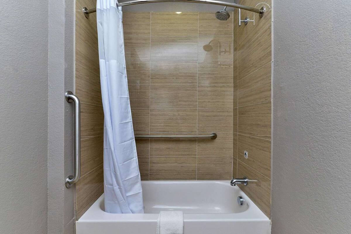 A walk-in shower with a white curtain, a grab bar, and a handheld showerhead.
