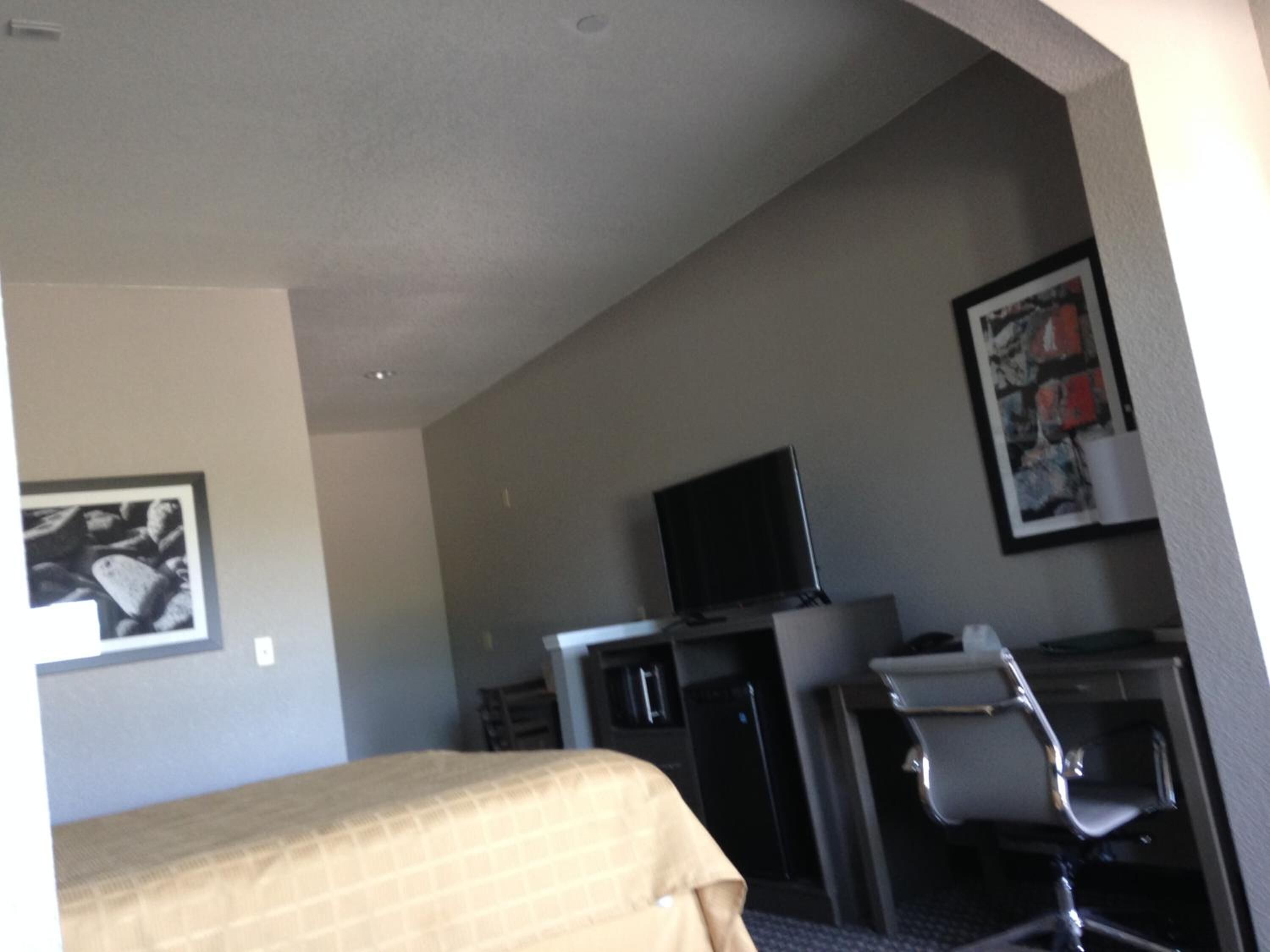 Una habitación de hotel con cama, escritorio, silla, televisor y refrigerador.
