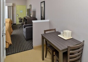 Habitación de hotel con una mesa de comedor, sillas, un refrigerador pequeño, un sofá y una alfombra estampada.