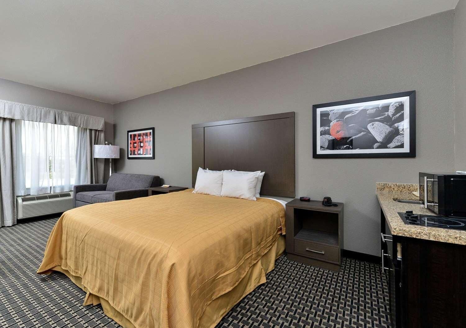 A hotel room with a large bed, a desk with a computer, a chair, a lamp, and two framed pictures on the wall.
