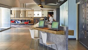 A modern reception area with a counter, two computer monitors, and a seating area with chairs and a sofa. - Ibis Culiacan (Culiacán)