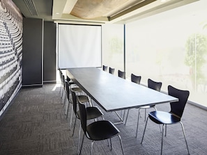 Una sala conferenze con un lungo tavolo e sedie, uno schermo per proiettore e ampie finestre.