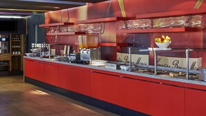 A buffet area with a red counter, various food stations, and a bowl of fruit on top. - Ibis Culiacan (Culiacán)