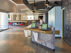 A modern reception area with a counter, two computer monitors, and a seating area with chairs and a sofa.