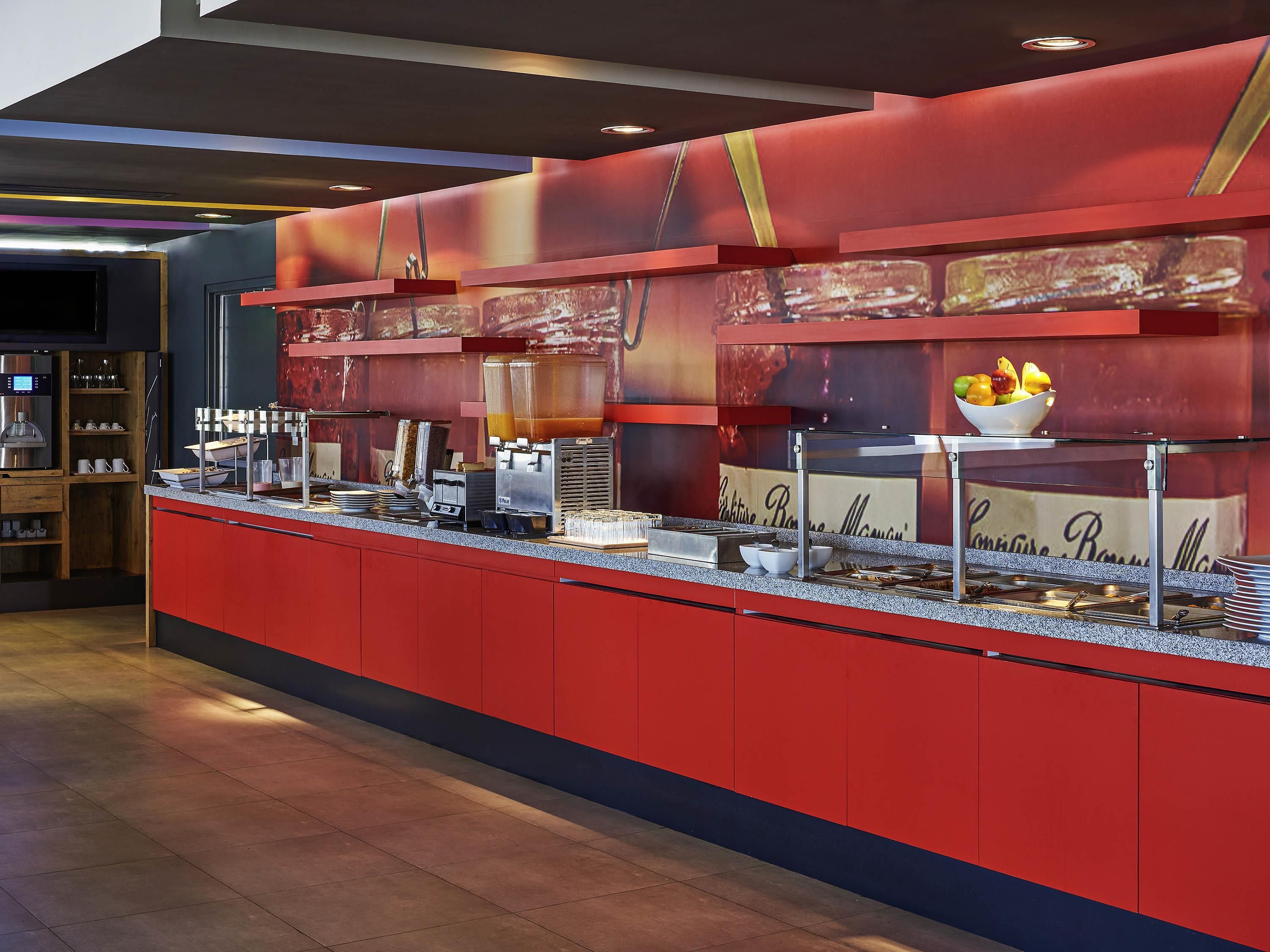 Een buffetgedeelte met een rode toonbank, diverse food stations en een schaal fruit.