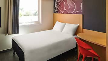 A hotel room with a bed, a desk, a chair, a window with curtains, and a wall with a decorative pattern.