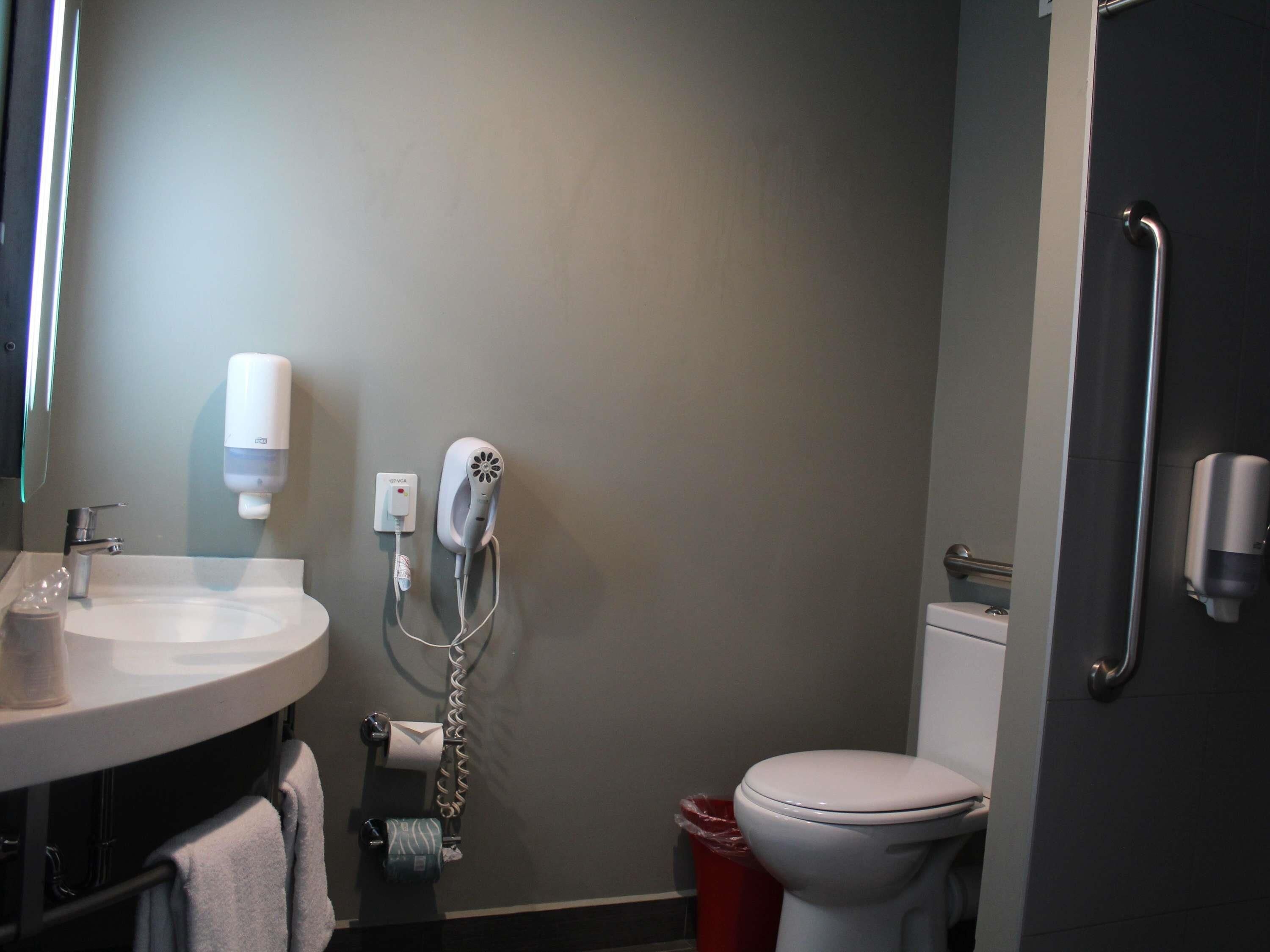 Casa de banho com lavatório, secador de cabelo, sanita e um contentor de lixo.