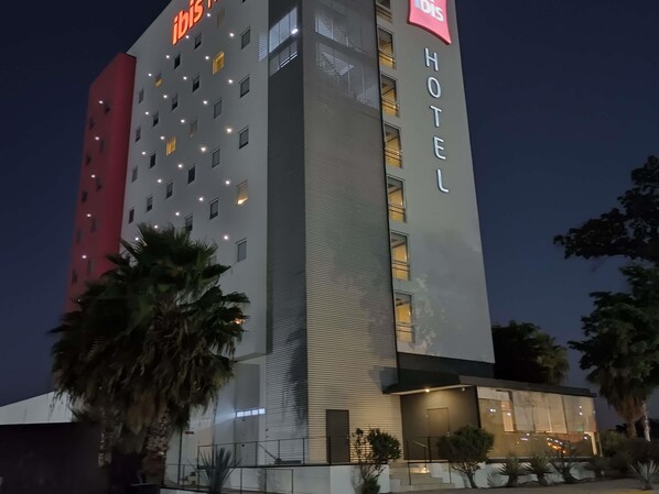 A modern hotel with a prominent "Ibis" sign, multiple floors, and a well-lit entrance.