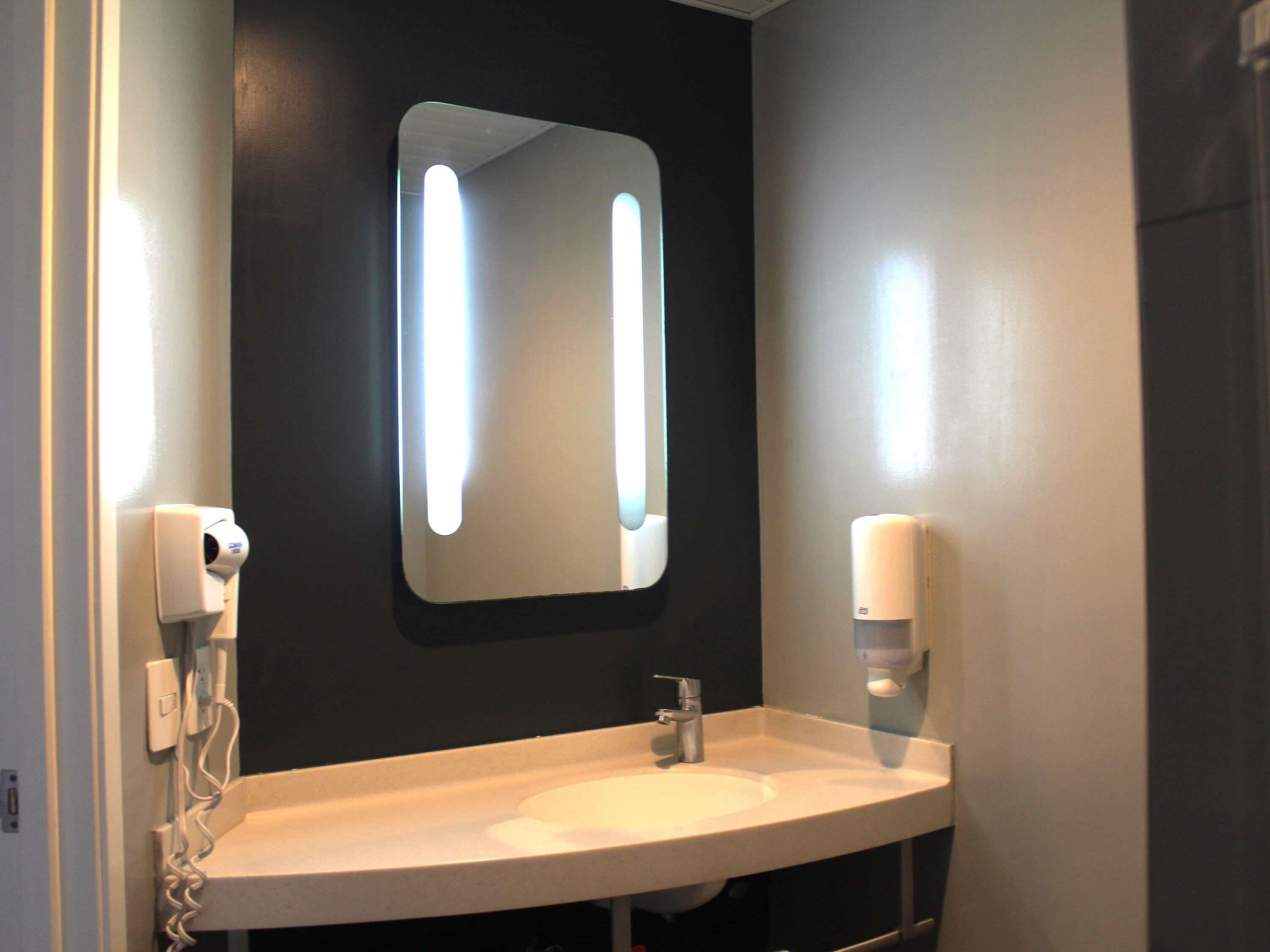 A bathroom with a white sink, a mirror, and two hand dryers.