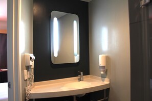 A bathroom with a white sink, a mirror, a hair dryer, and a soap dispenser. - Ibis Culiacan (Culiacán)
