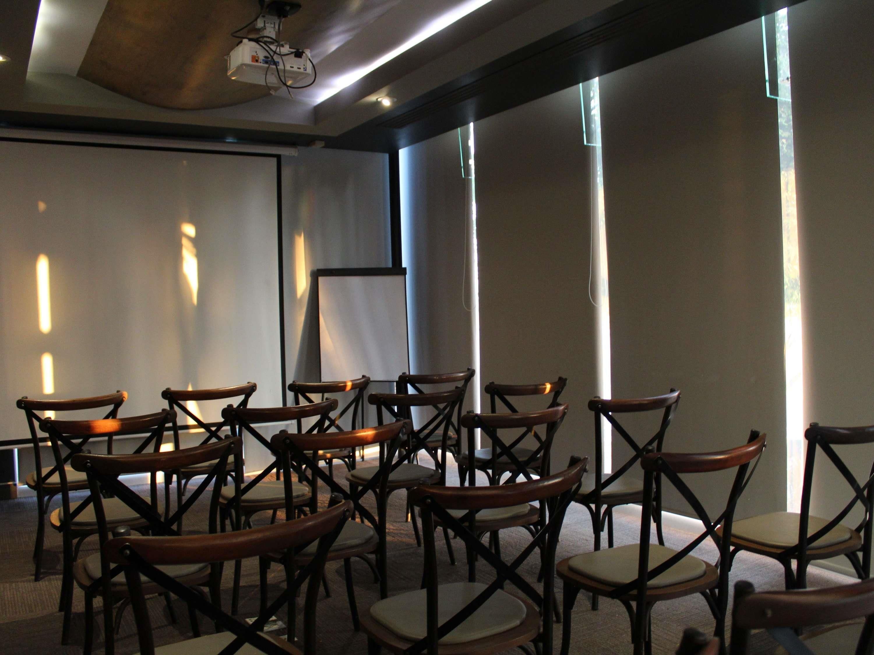 Uma sala de conferência com fileiras de cadeiras de madeira, um projetor e uma tela.