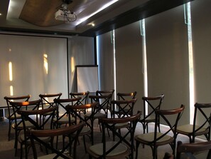 Un salón de conferencias con filas de sillas de madera, un proyector y una pantalla.