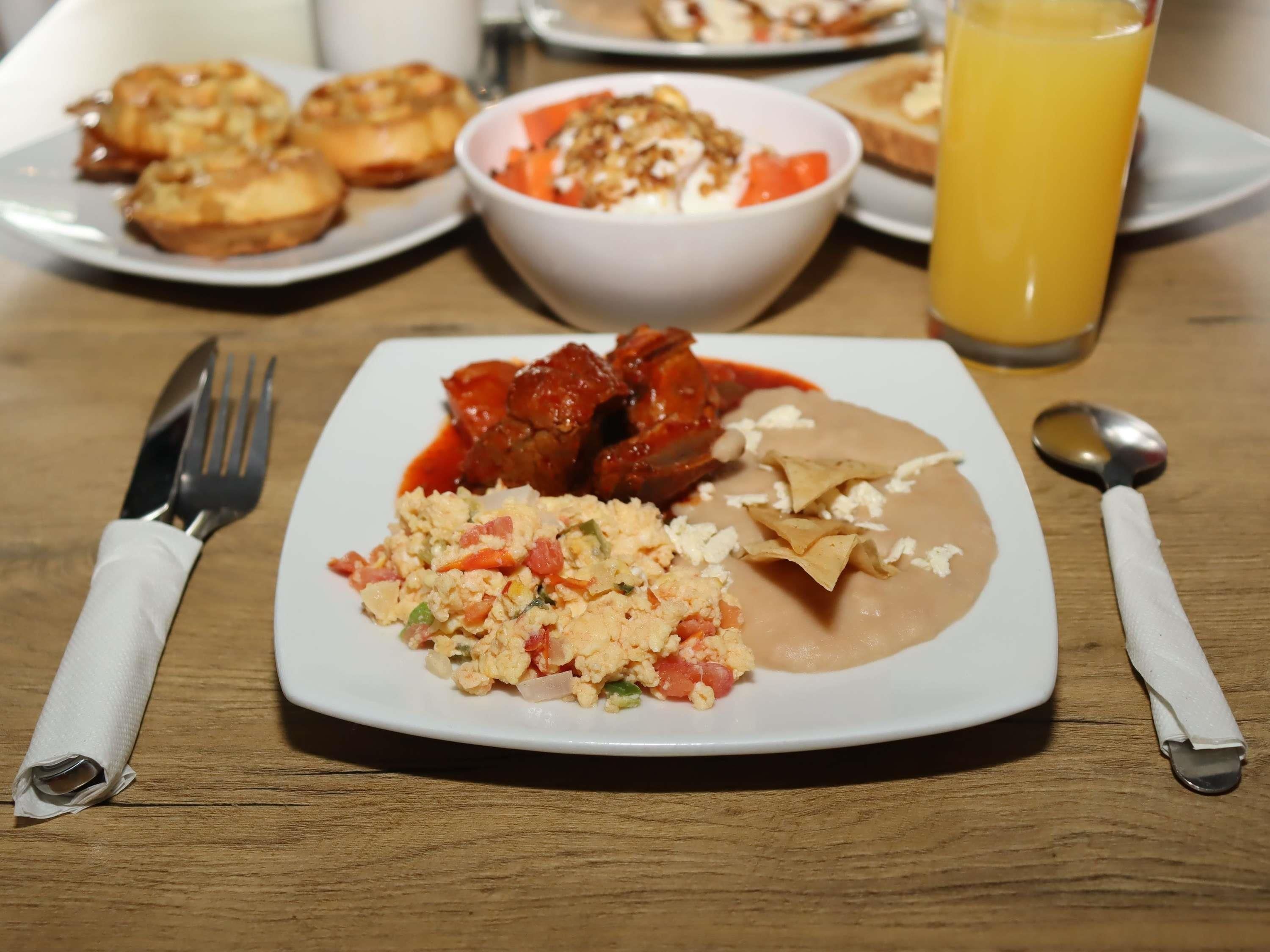A plate of food with scrambled eggs, refried beans, and meat, accompanied by a glass of orange juice.