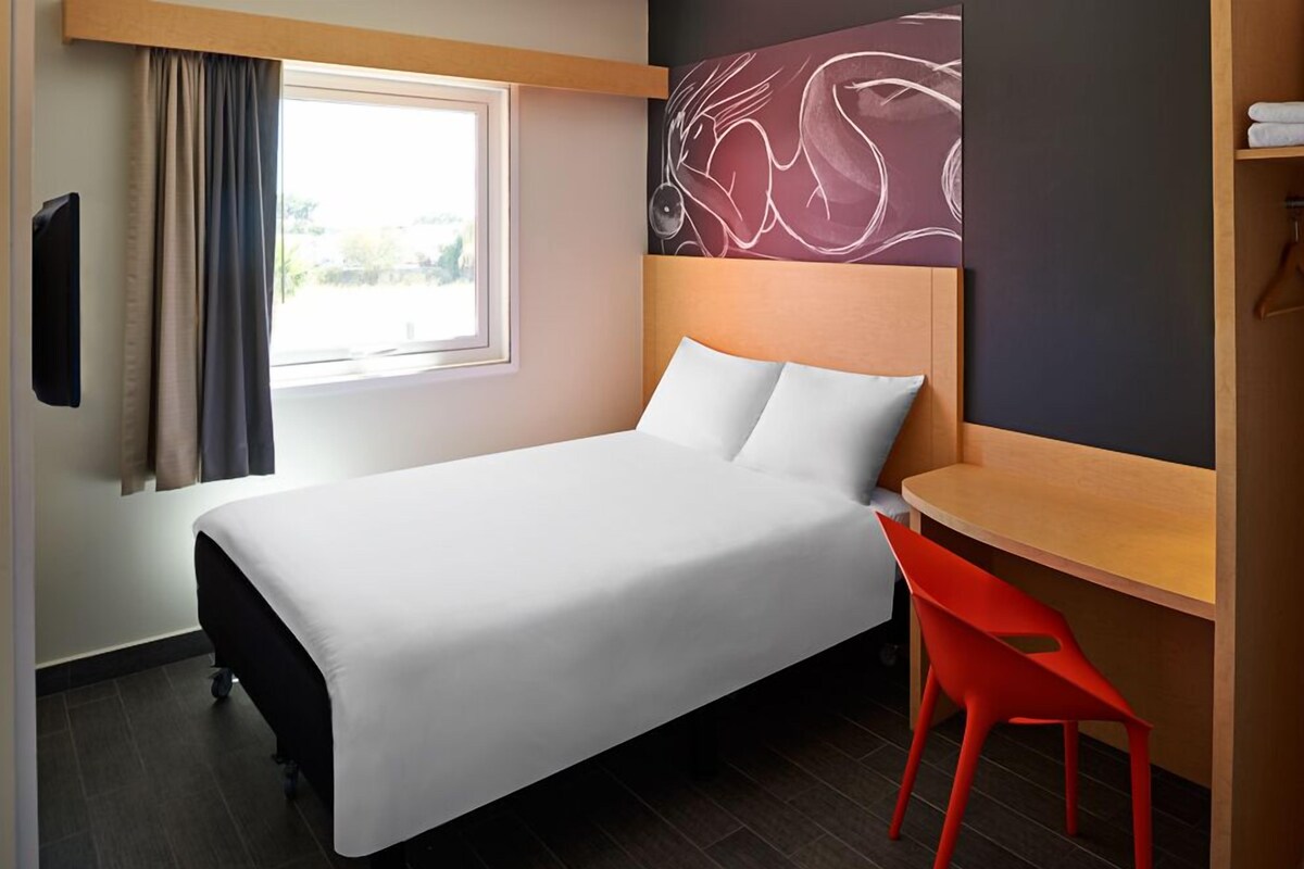 A hotel room with a bed, a desk, a chair, a TV, and a window with curtains.
