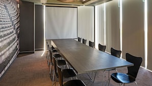 A conference room with a long table and chairs, large windows, and a patterned wall.