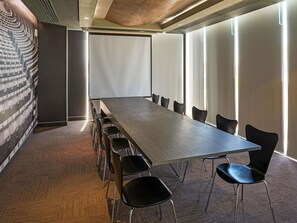 A conference room with a long table and chairs, large windows, and a patterned wall.