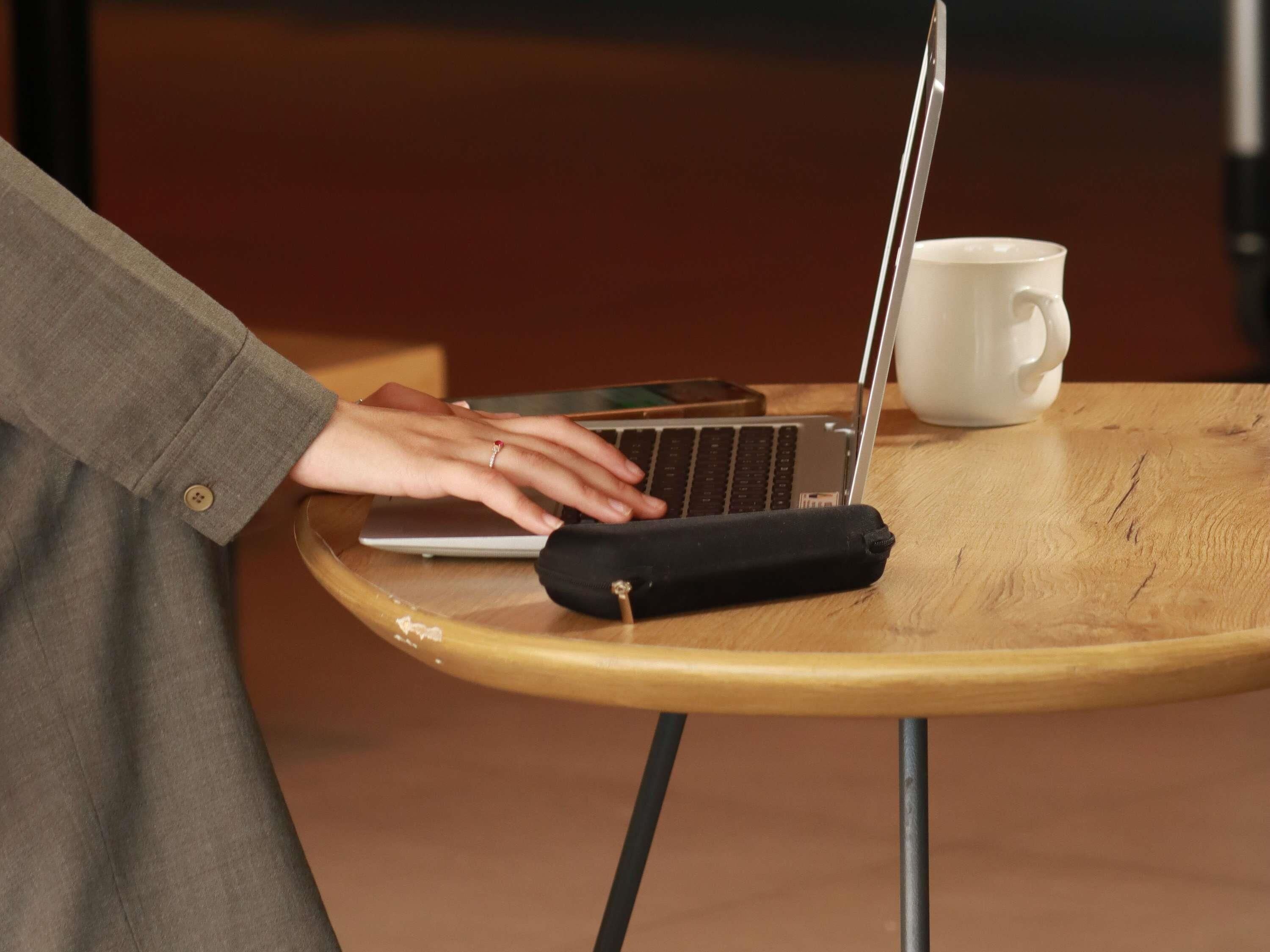 Una persona usando una computadora portátil sobre una mesa de madera con una taza blanca a su lado.