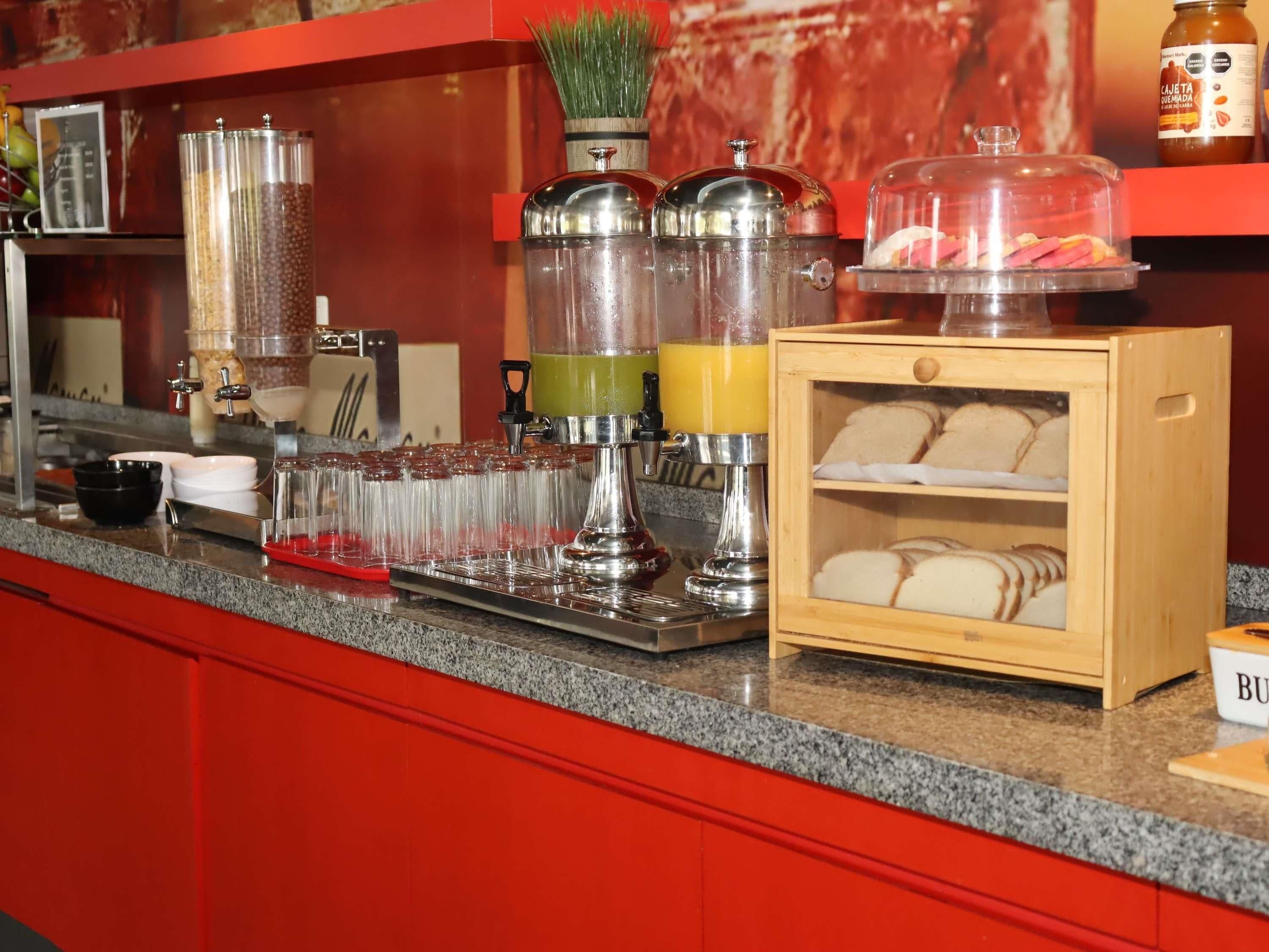 Una barra de desayuno con máquinas de café, dispensador de zumo y exhibición de pan.
