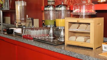 Una barra de desayuno con máquinas de café, dispensador de zumo y exhibición de pan.