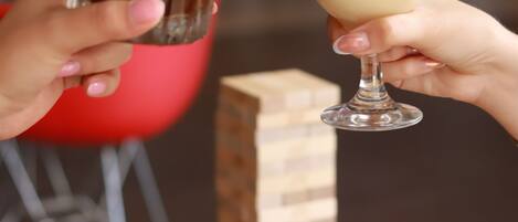 Two hands holding glasses of a beverage, a red chair, and a small bowl of popcorn in the background.