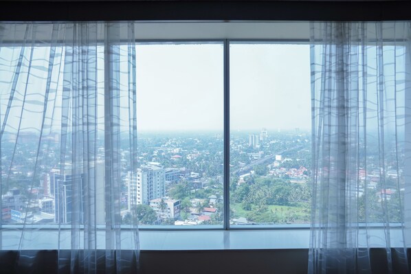 A large window with sheer curtains, offering a view of a cityscape with buildings and greenery.