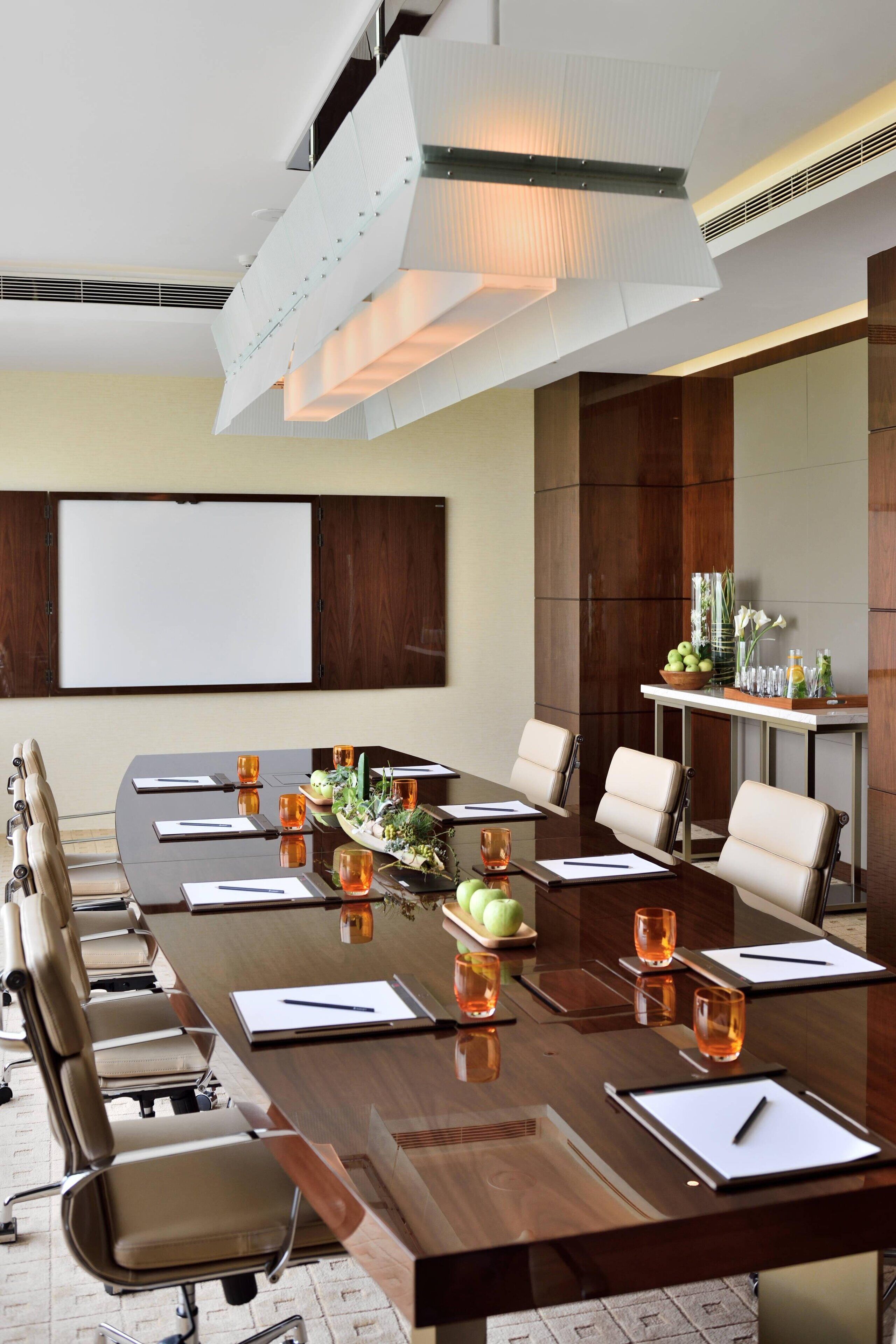 A conference room with a long table, chairs, a projector screen, and a small table with decorative items and drinks.