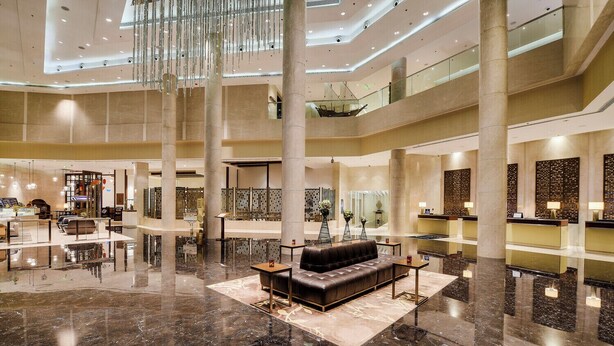A spacious lobby with a central seating area, multiple reception desks, and a high ceiling with hanging lights. - Kochi Marriott Hotel (Kanayannur)
