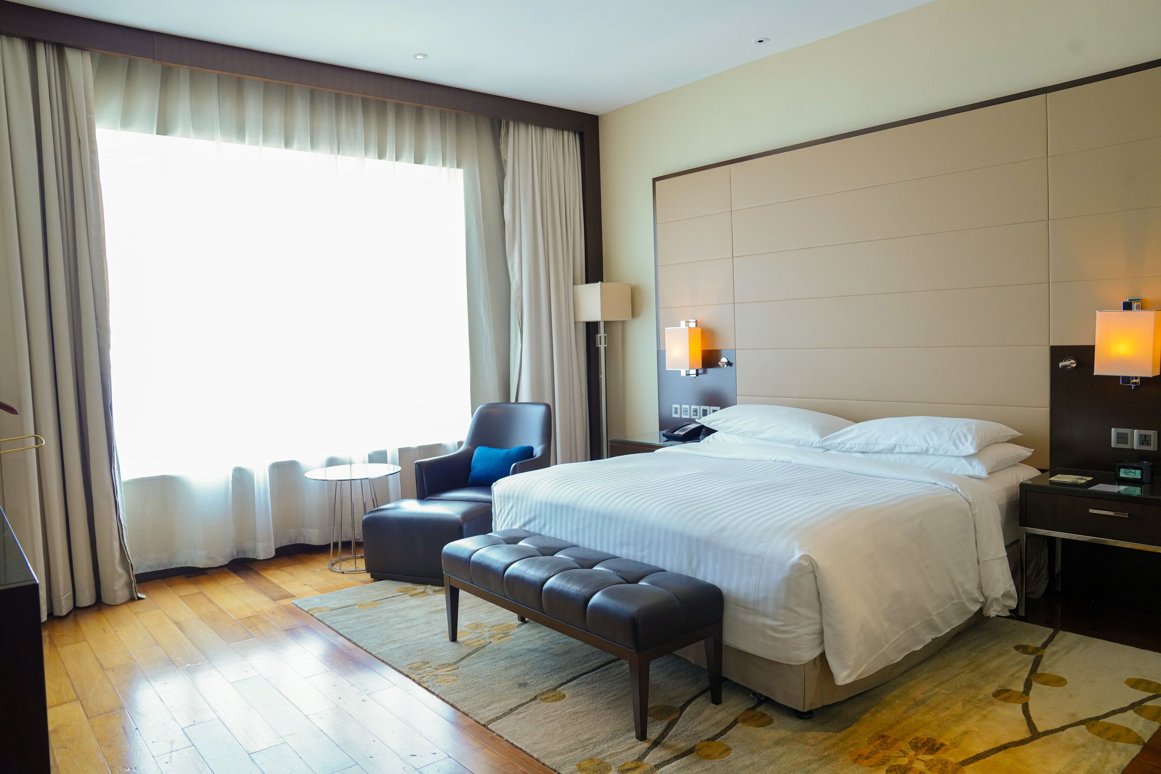 Una habitación de hotel con una cama grande, una silla, una mesita y un banco.
