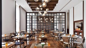 A restaurant with wooden tables and chairs, a decorative wall, and hanging spherical lights. - Kochi Marriott Hotel (Kanayannur)
