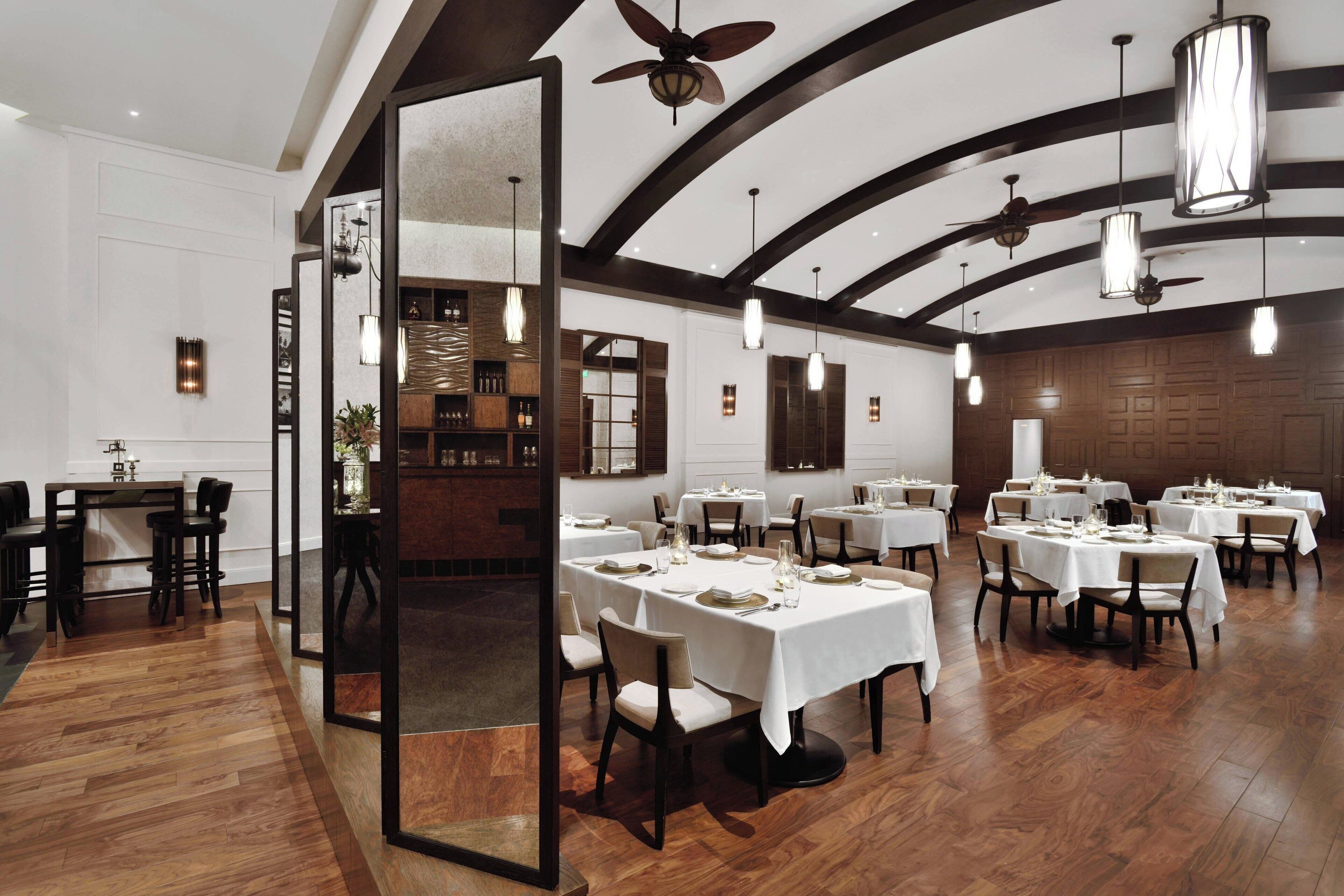 Un restaurant avec de nombreuses tables dressées pour le service, un plancher en bois et des ventilateurs de plafond.