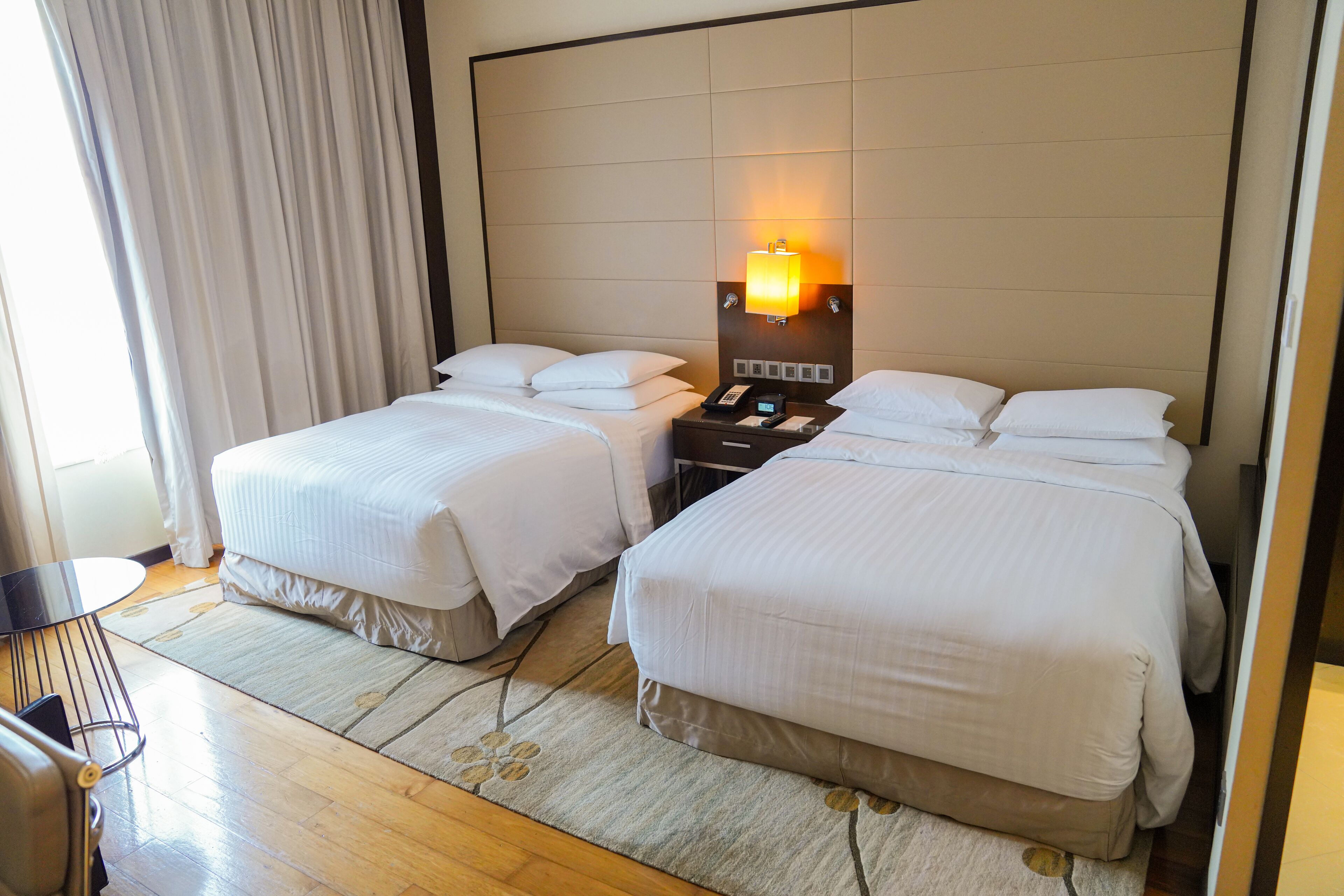 A hotel room with two beds, a bedside table with a lamp, a phone, and a chair.