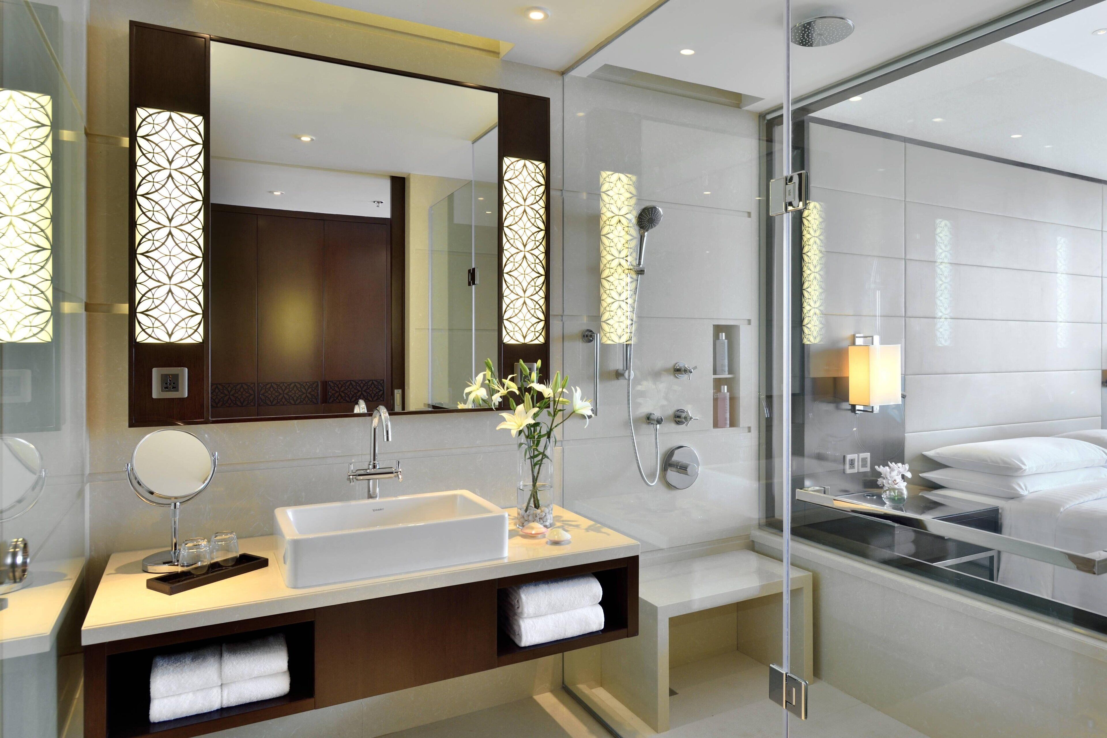 A modern bathroom with a large mirror, a sink, a shower, and a glass-enclosed shower area.