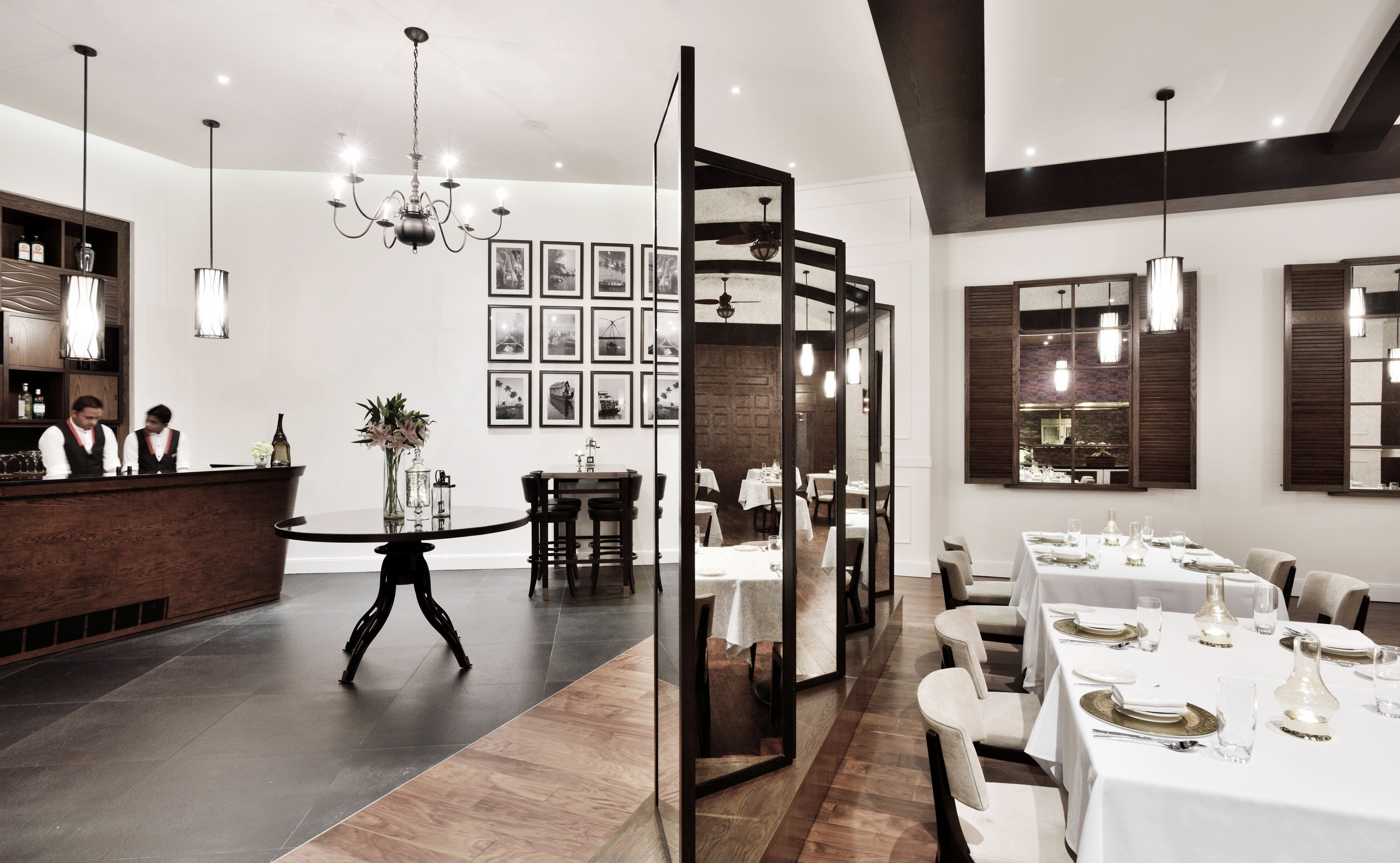 A modern restaurant interior with a bar area, dining tables set for service, and a chandelier.