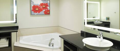 A modern bathroom with a bathtub, a sink, and a large mirror. There is a framed picture of flowers on the wall.
