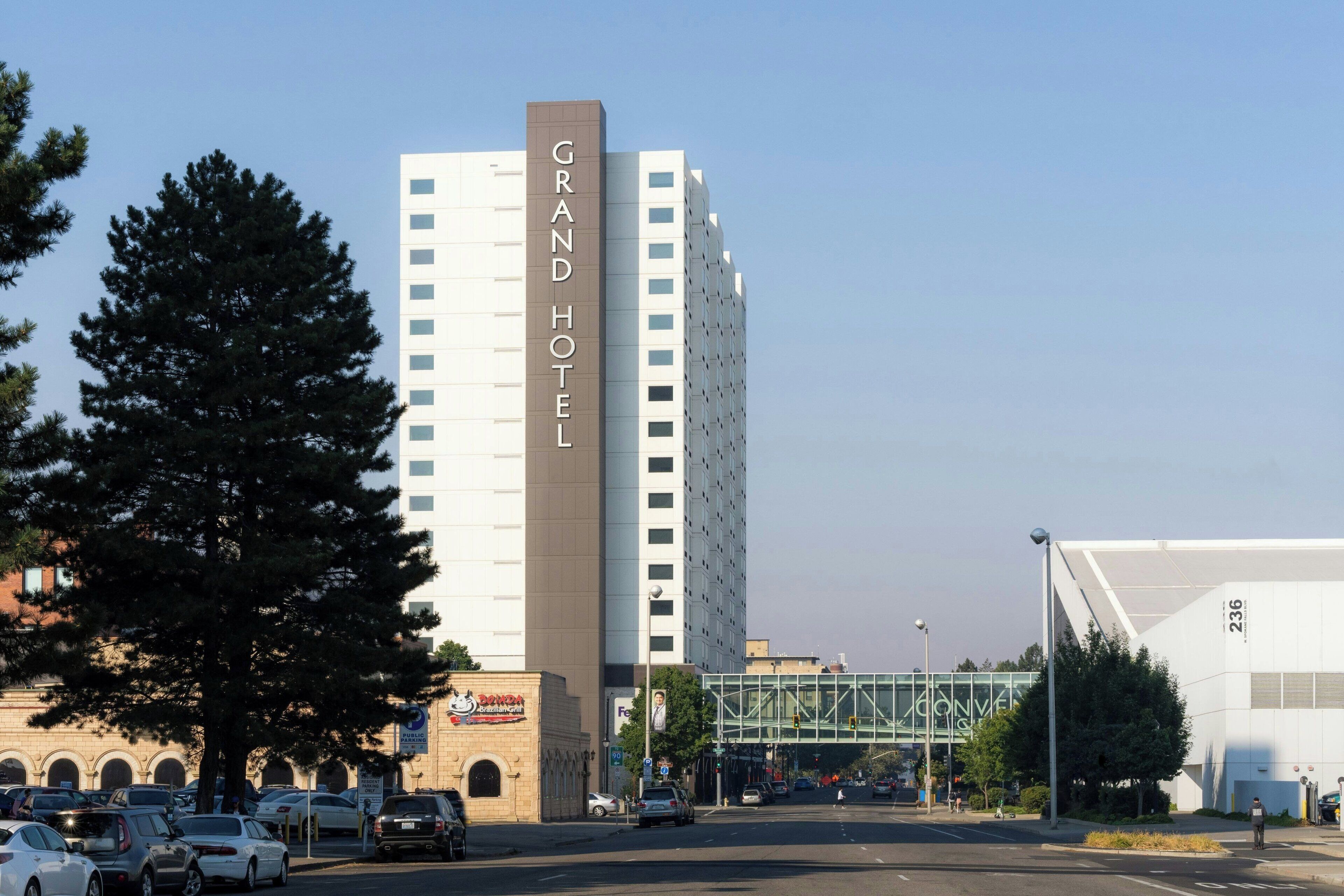 A Grand Hotel building with a prominent sign, a parking lot with cars, and a pedestrian overpass in the background.