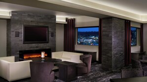 A modern living room with a fireplace, comfortable seating, a large TV, and a view of the city at night. - The Davenport Grand, Autograph Collection (Spokane)