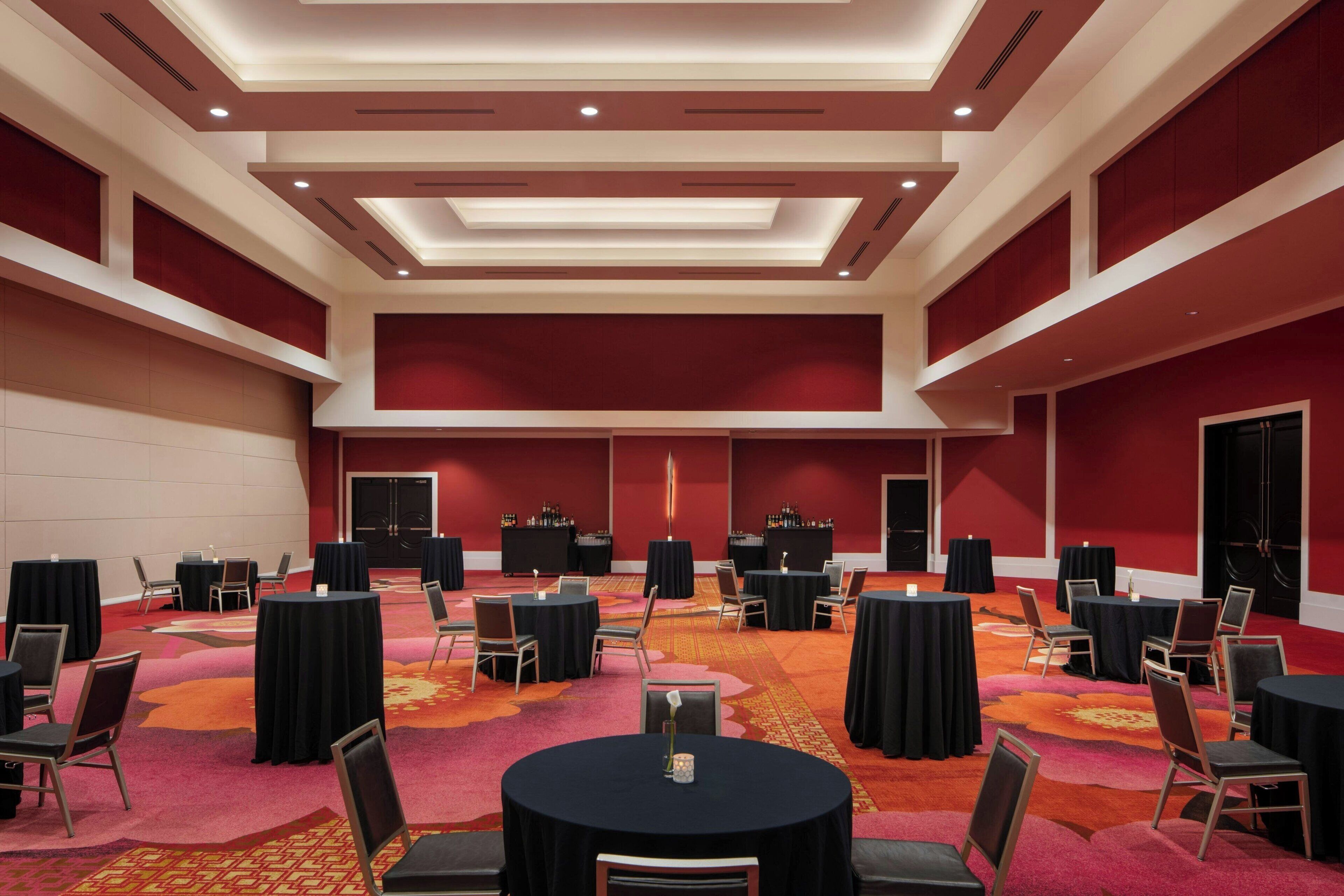 Une salle de conférence dotée de plusieurs tables et chaises, d’un tapis à motifs et d’une décoration aux couleurs rouge et blanche.