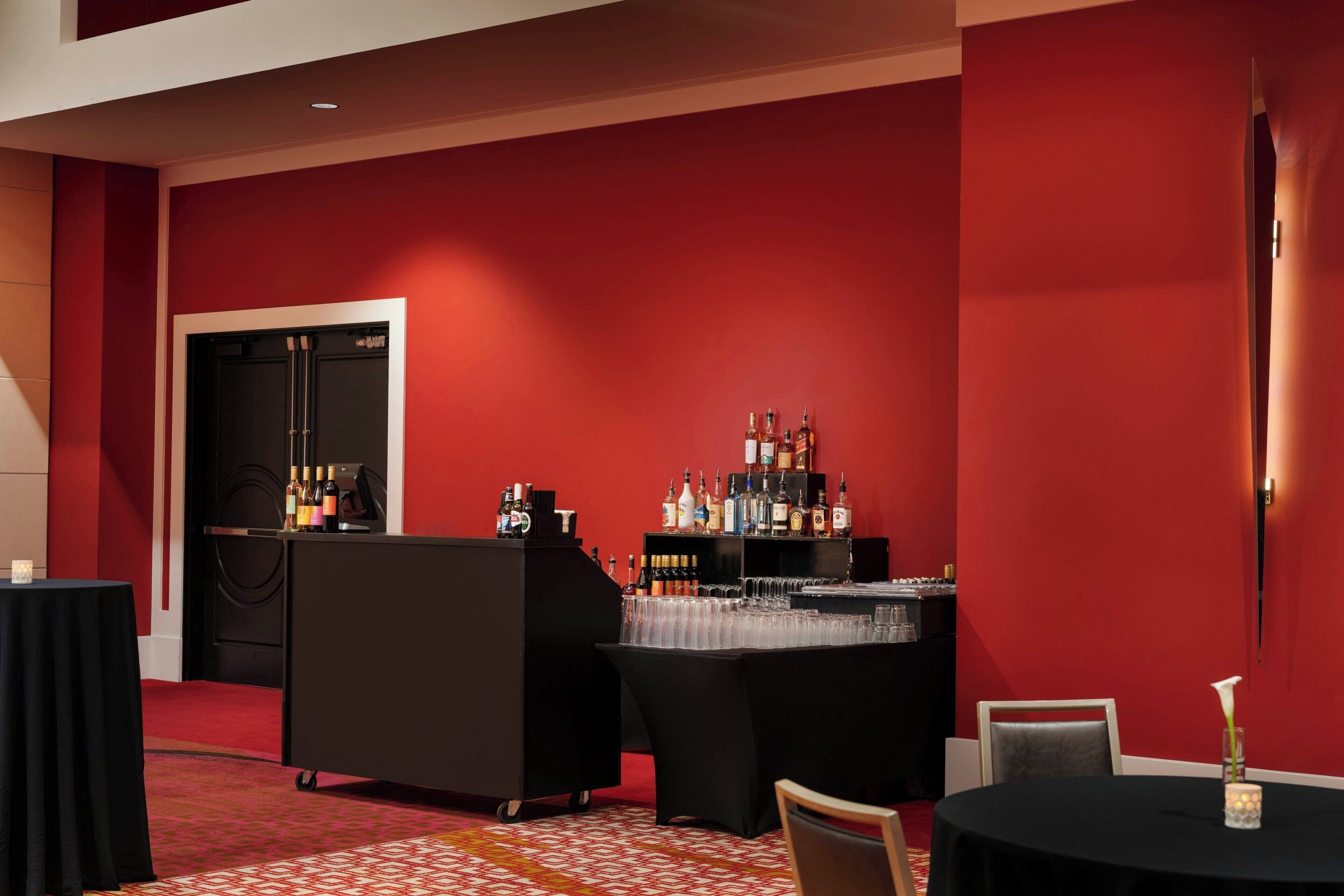 A bar area with a red wall, black furniture, and a variety of bottles and glasses.
