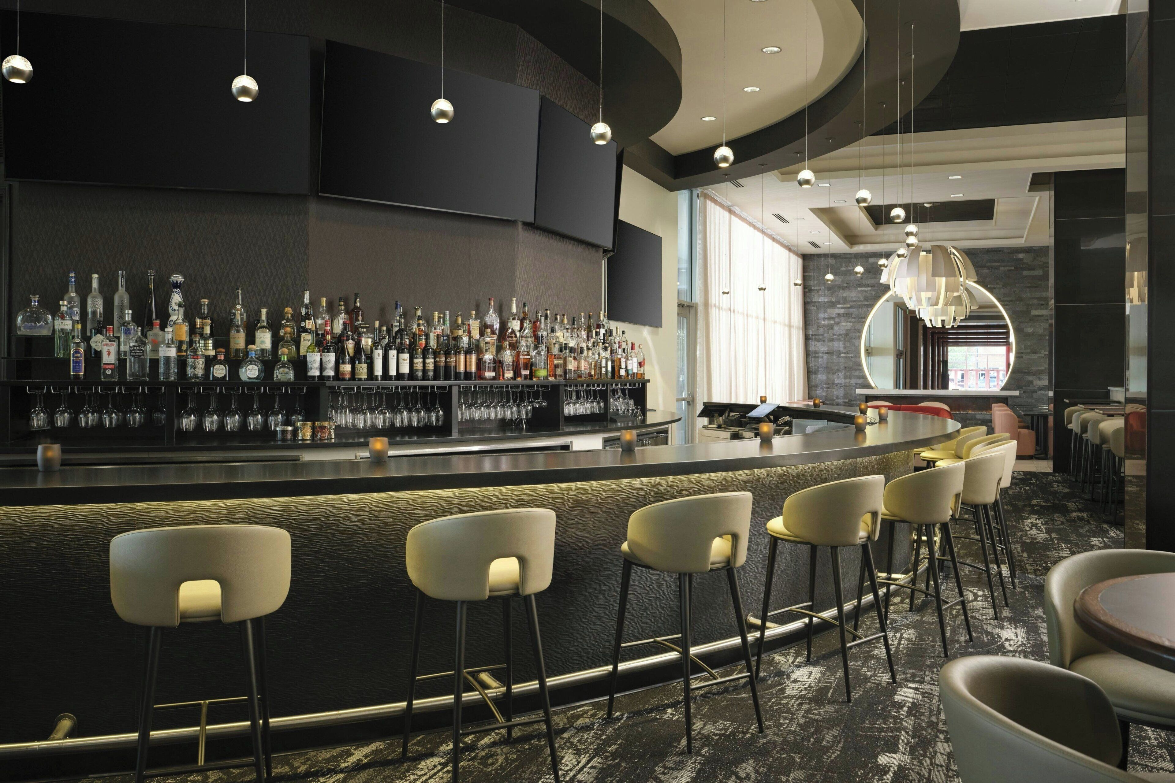 A bar area with a long counter, multiple stools, and a variety of liquor bottles.