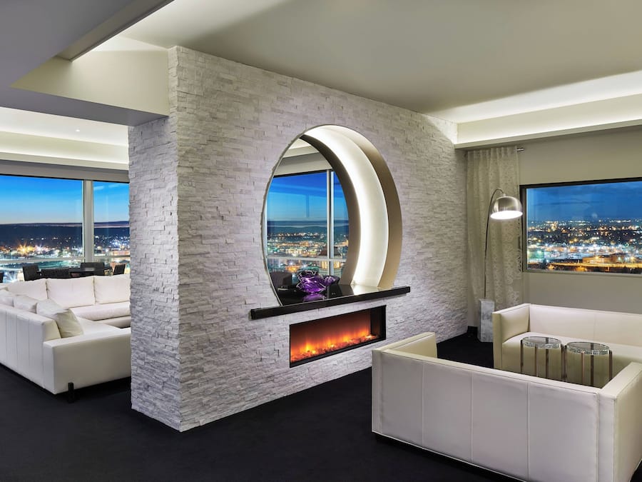 A modern living room with a fireplace, white sofas, and a large window offering a city view.