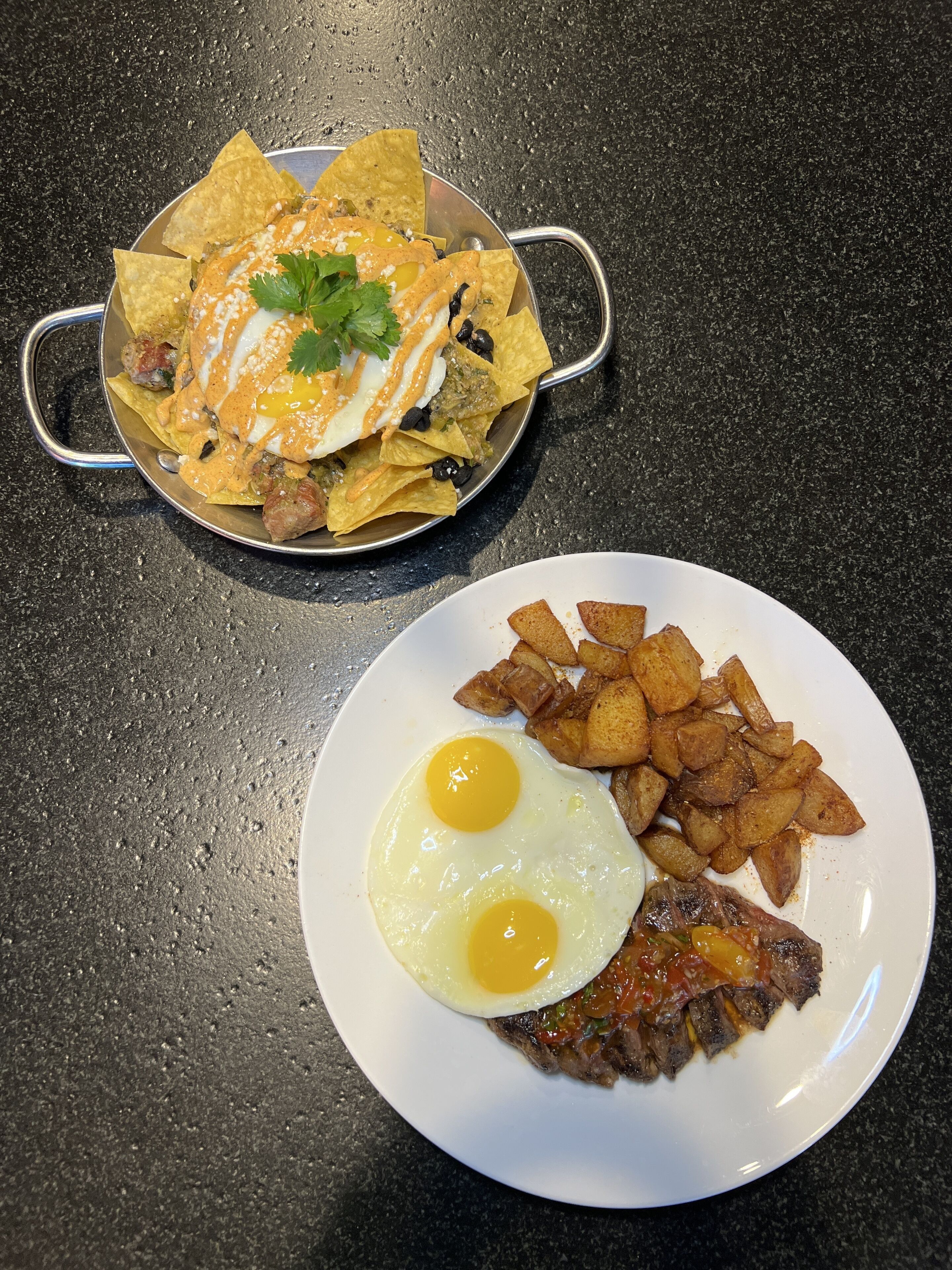 A plate with two fried eggs and a steak, and a bowl of nachos with cheese and jalapeños.